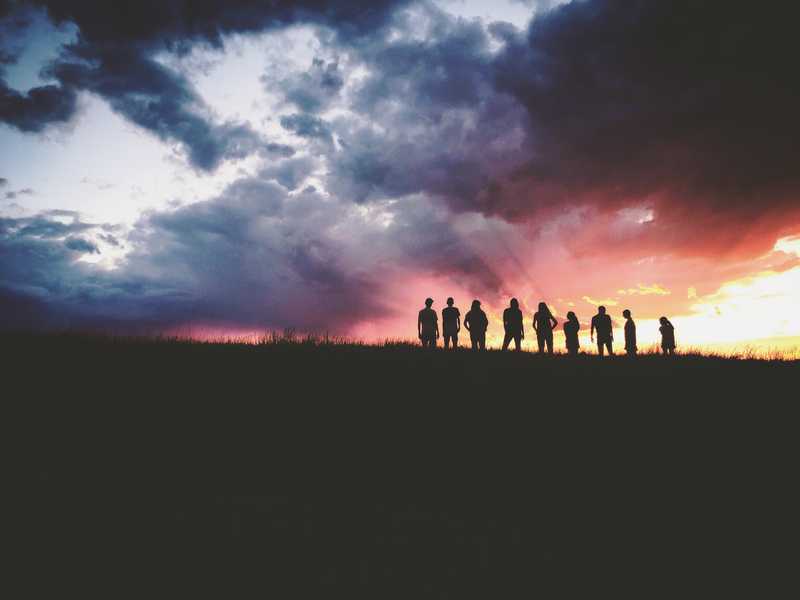 A group of people on top of a hill with the sunset behind them